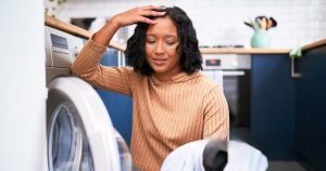 Frustrated woman sitting near a dryer, dealing with a dryer not heating – Troubleshooting and repair tips for fixing dryer heating issues